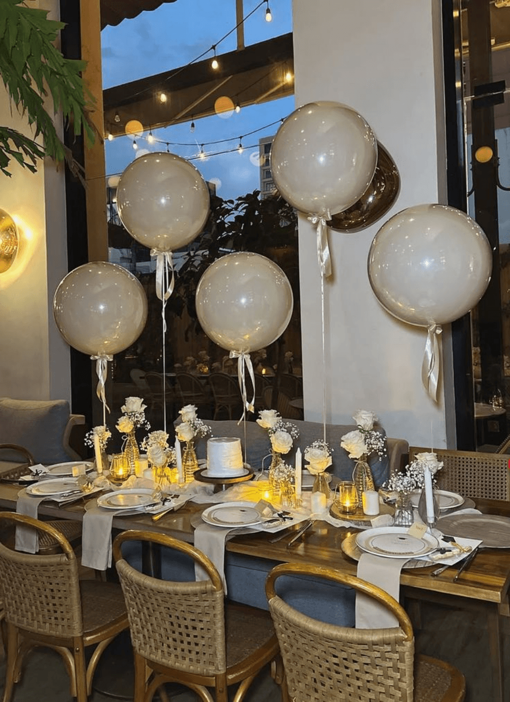 A candlelit table set beneath oversized balloons and hanging greenery
