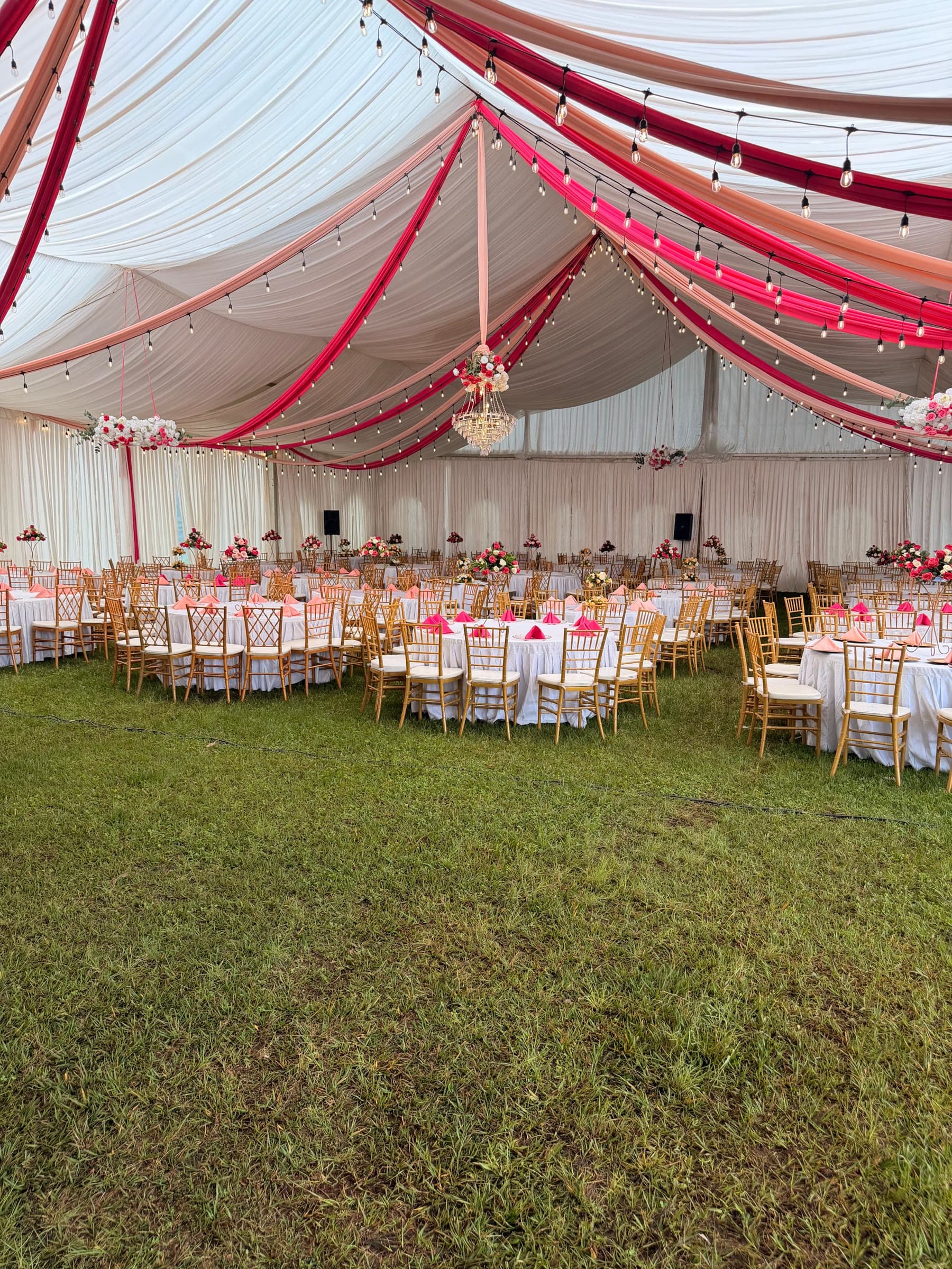 Cream, coral and fuchsia fabric draped across the marquee ceiling above tables set for dinner